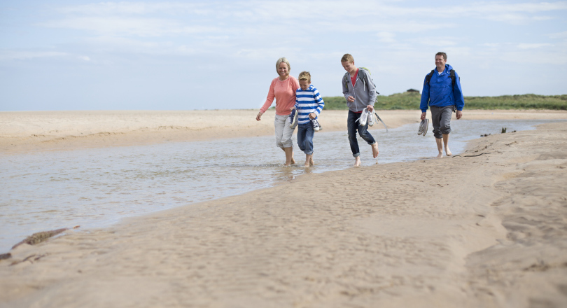 Family of four walk on a beach in the UK